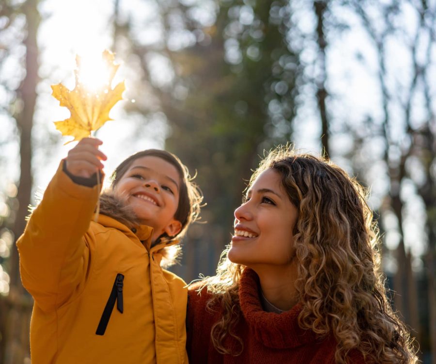 Beautiful mother looking at a leaf her son is holding on a sunny autumn day at the park - Lifestyles